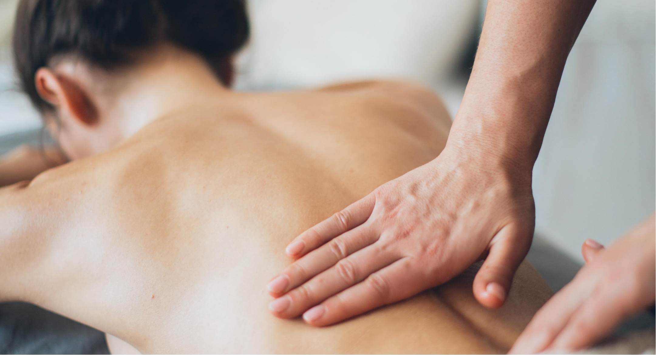 Image of woman lying down face forward, receiving a back massage to relief muscle aches and pains.